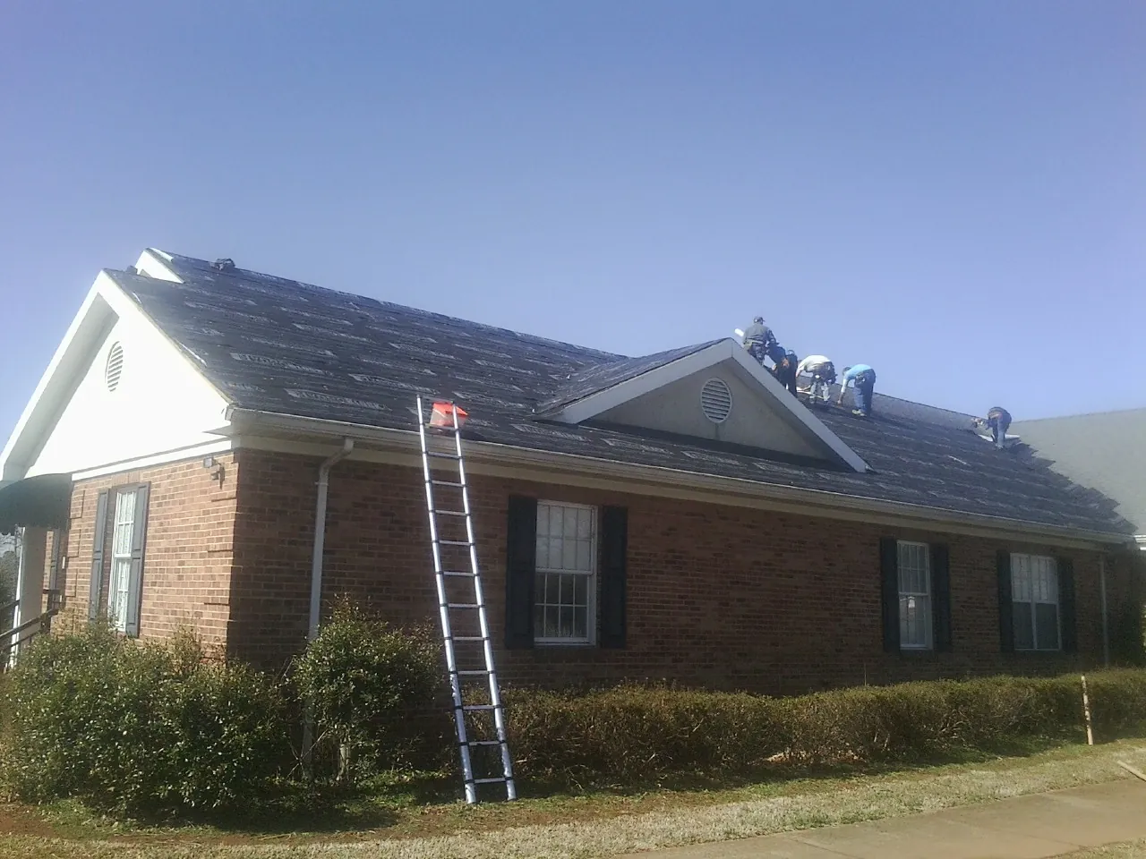 Crew tearing shingles off a brick ranch roof with a ladder set — Metal Roof Repair work by our crew in Tornado