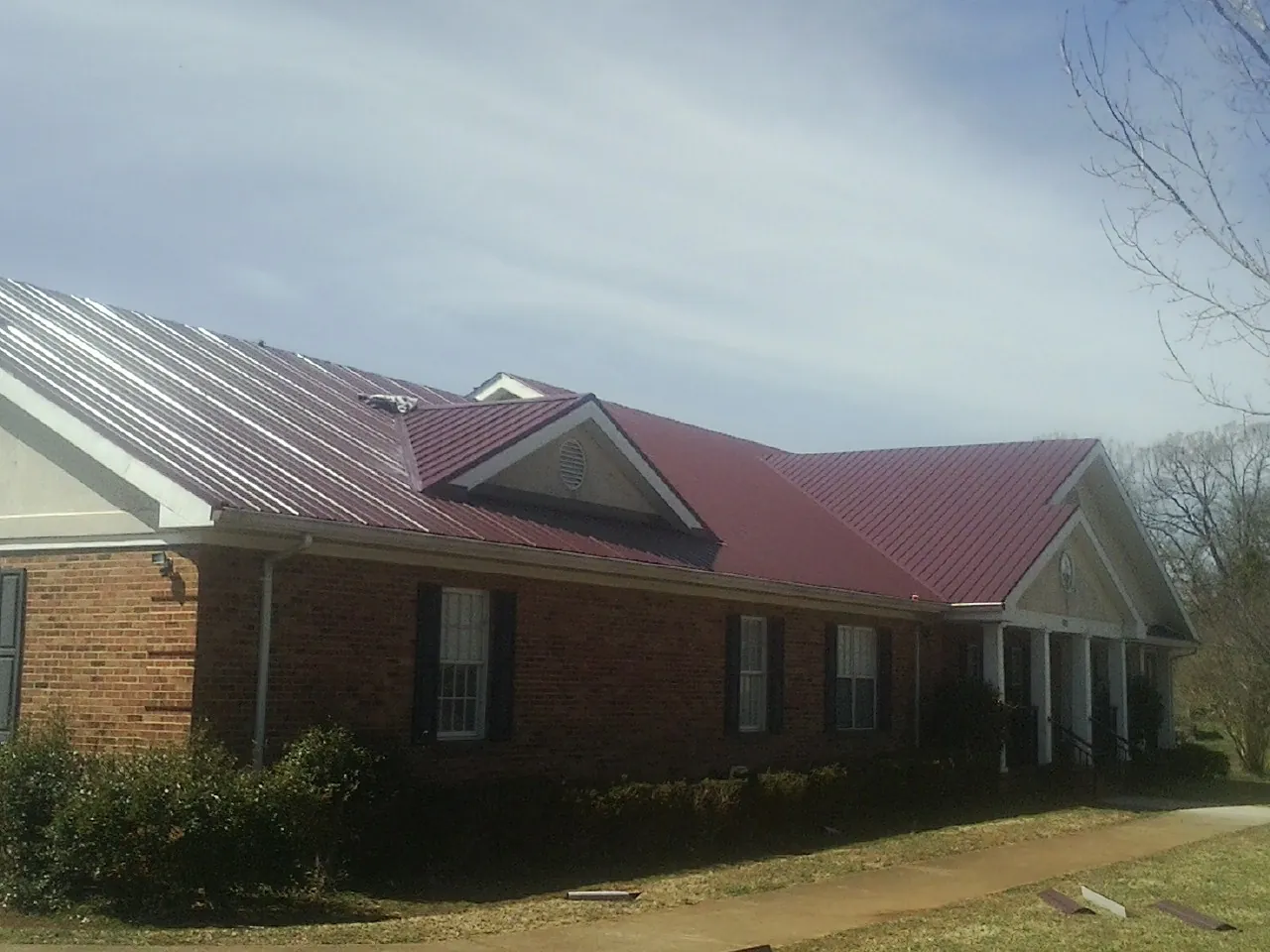 Red metal roof with gabled entries on a long brick building, from a Hail Damage Roof Repair job in Tornado