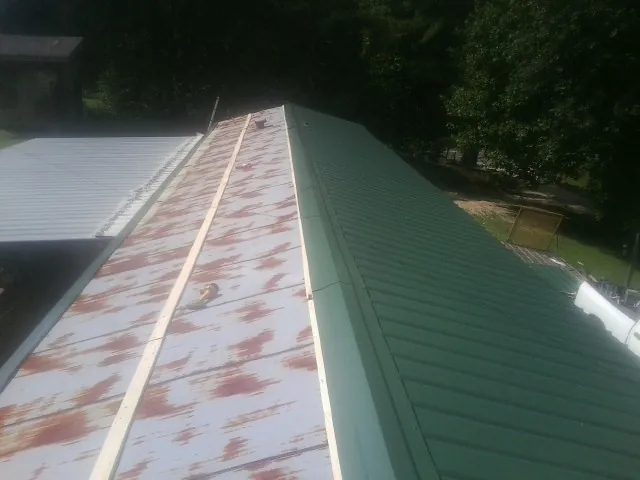 Old rusted panels beside newly installed green metal roofing — Wind Damage Roof Repair by Roofing Brothers in Tornado