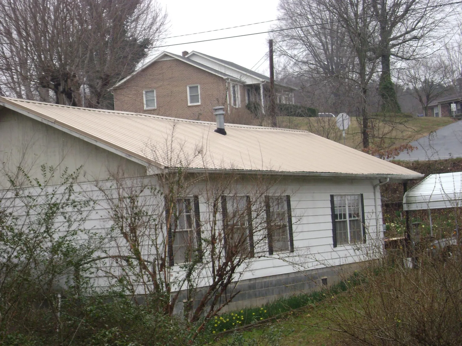 Tan metal roof on a white sided house set into a hillside — Commercial Roofing by Roofing Brothers in Tornado