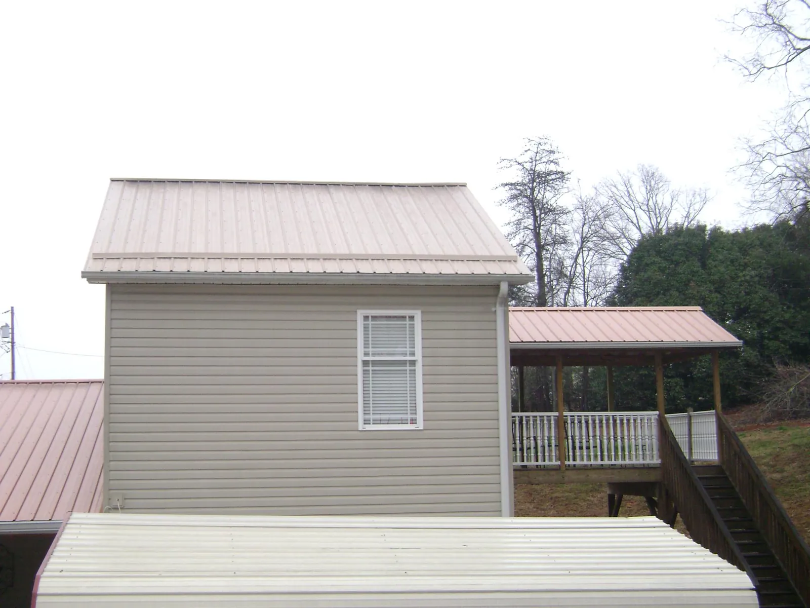 Tan metal roofs on a two story addition and attached porch, from a Roof Replacement job in Tornado